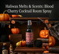 Haliwax Blood Cherry Cocktail Halloween room spray bottle displayed on a dark wooden surface surrounded by pumpkins, jack-o-lanterns, cobwebs and spooky Halloween props.