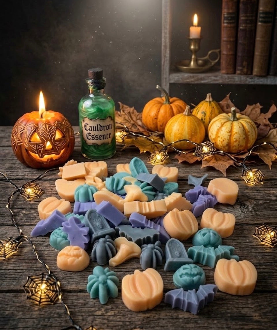 Assorted Halloween shaped wax melts in orange, blue and purple scattered on a rustic wooden surface with jack-o-lanterns, pumpkins, fairy lights and a cauldron essence bottle.