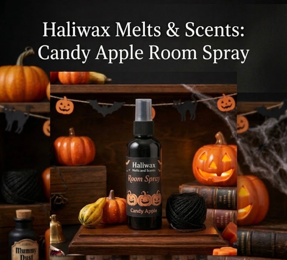 Haliwax Candy Apple Halloween room spray bottle displayed on a dark wooden surface surrounded by pumpkins, jack-o-lanterns, cobwebs and spooky Halloween props.