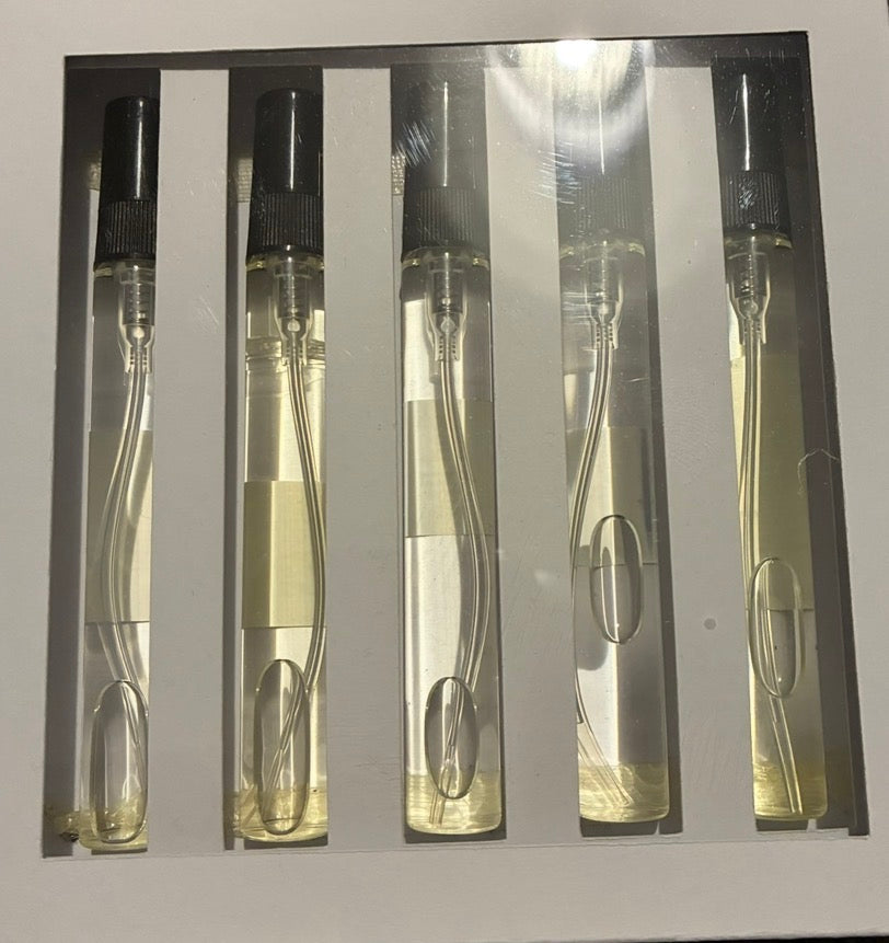 Five clear glass perfume sample vials with black spray tops arranged in a white box with vertical slots.